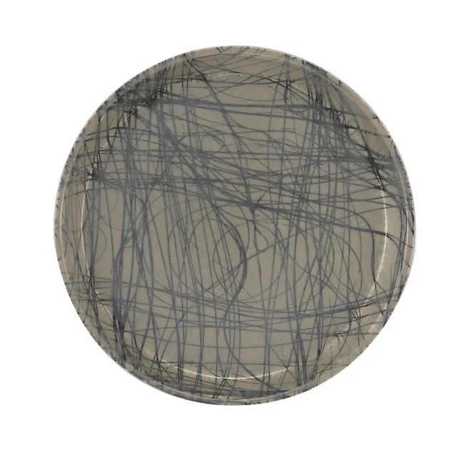 A round fiberglass tray with a beige background features an abstract design of intersecting, dark gray scribble lines, creating a chaotic, modern pattern. Durable and dishwasher safe, the plate is photographed against a plain white background.