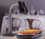 A buffet setup features a stainless steel Double Heat Lamp with an adjustable neck, warming trays of sliced roast beef and cheesy casserole. Plates are stacked on a dressed dining table with empty glasses in a modern restaurant setting.