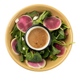 A yellow melamine bowl, both temperature resistant and dishwasher safe, holds a green salad with spinach and pink watermelon radish slices around a cup of vinaigrette, set against a white background.