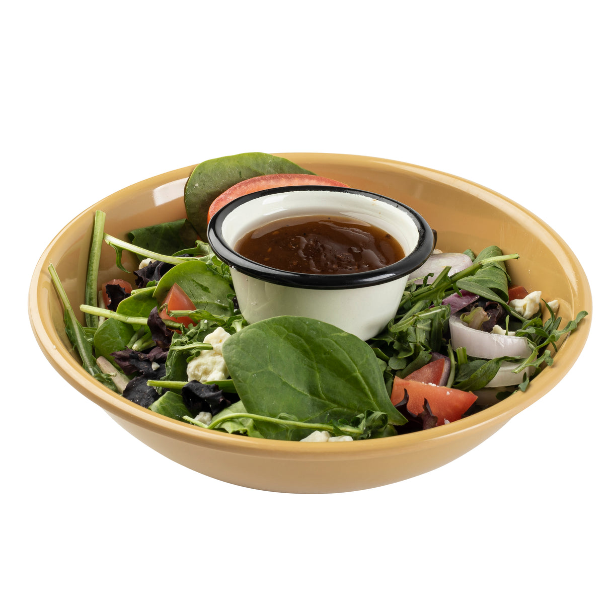 A tan melamine bowl filled with fresh salad greens, spinach leaves, tomato wedges, olives, red onion, and feta cheese. A small enamel cup of brown salad dressing sits in the center. Both are dishwasher safe for easy cleanup. The background is plain white.