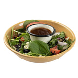 A tan melamine bowl filled with fresh salad greens, spinach leaves, tomato wedges, olives, red onion, and feta cheese. A small enamel cup of brown salad dressing sits in the center. Both are dishwasher safe for easy cleanup. The background is plain white.