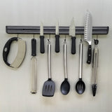 A wall-mounted magnetic holder keeps kitchen tools—mezzaluna chopper, grater, knives, spatula, spoons, and tongs—neatly arranged in a row, perfect for a cash & carry setup or organized home cooking space.