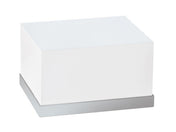 A white rectangular box with smooth edges sits on a flat, stainless steel base. This minimalist Luxe Display Riser is unmarked and photographed against a plain white background.