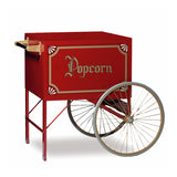 A vintage-style red popcorn cart by Gold Medal Products features gold accents, decorative Popcorn lettering, two large spoked wheels, small supporting legs, a black handle, ornate trim, and a convenient storage compartment—perfect for old-fashioned carnival flair.