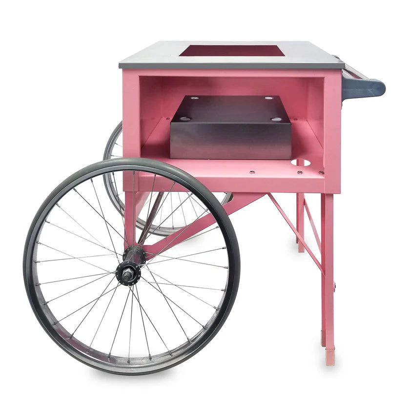 A Gold Medal Products Pink Floss Cart features two large spoked wheels, a flat top surface, and an open compartment below with a rectangular block inside. This floss unit cart includes a handle on one end and two legs on the other.