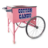 A Pink Floss Cart with large metal wheels and handle. The cart features bold, blue, vintage-style COTTON CANDY lettering on the side. Made by Gold Medal Products, this floss unit cart has a flat top with an opening and stands on four legs.