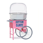 A Pink Floss Cart by Gold Medal Products, featuring large metal wheels, a rectangular base labeled “COTTON CANDY” in bold blue letters, a clear dome for displaying treats, and a sturdy handle. Includes a stainless steel spacer for added durability.
