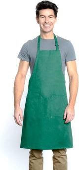 A smiling man with short dark hair wears a gray t-shirt, tan pants, and a chef-approved green bib apron with two front pockets and an adjustable neck. He stands against a plain white background with his arms relaxed at his sides.