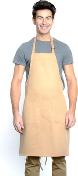 A smiling man with short dark hair wears a chef-approved bib apron with an adjustable neck over a grey t-shirt and tan pants. He stands facing forward against a plain white background, arms relaxed by his sides.