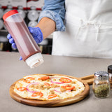 A person in a white apron and blue glove uses an NSF squeeze dispenser to add sauce onto a pizza with tomato, onion, and cheese on a wooden tray. Two shakers are on the gray countertop; all items are dishwasher safe for easy cleaning.