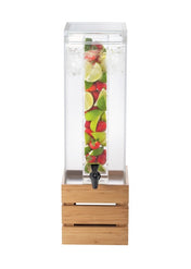 A tall, clear beverage dispenser filled with water and ice features a BPA free infusion chamber packed with cut strawberries, lime, and green apple slices. The black spigot and wooden crate-style base complete its refreshing display.