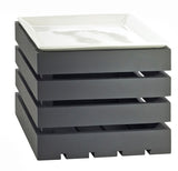 A white, square ceramic plate sits atop the modern Midnight Bamboo Crate Riser—a black, slatted shelf riser with four stacked layers and evenly spaced gaps, resembling a display basket with a solid base.