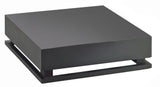 A minimalist, matte black square metal crate riser sculpture with a thick top resting above a matching base, creating a narrow gap between the layers, is showcased against a plain white background.