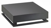 A minimalist, matte black square metal crate riser sculpture with a thick top resting above a matching base, creating a narrow gap between the layers, is showcased against a plain white background.