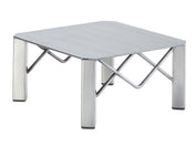 A small, square metal table with a polished finish, flat gray surface, four thick legs, and diagonal support bars connecting the legs beneath the tabletop in an X-shaped pattern. The table boasts a minimalist, industrial design inspired by Industrial Risers.