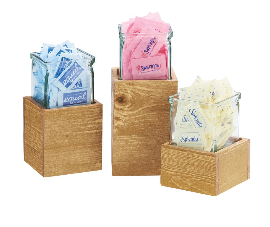 Three glass jars in rustic pine Madera Single Jar Risers display sweetener packets: blue Equal, pink Sweet'n Low, and yellow Splenda. The containers sit at varied heights, with each sweetener clearly visible.