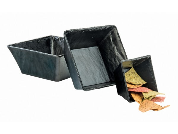 Three square, black, stone-like melamine bowls of varying sizes are arranged in a staggered, diagonal line. The smallest bowl contains assorted colored triangular chips, while the two larger bowls are empty. The bowls have a textured, handcrafted appearance.