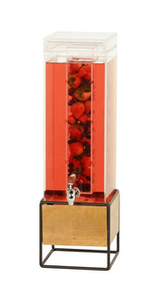 A tall, clear 3 gallon Madera Beverage Dispenser filled with red liquid and whole strawberries, raspberries, and blueberries. The infusion chamber sits on a gold and black metal stand, featuring a silver spigot at the bottom for pouring.