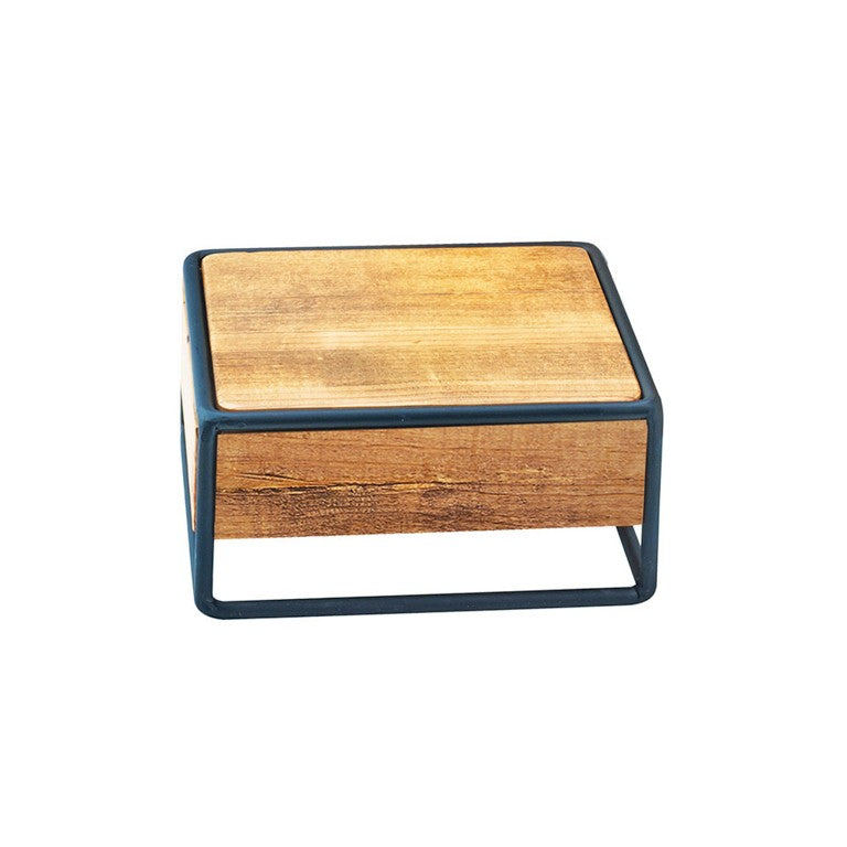 A small, square, wooden box crafted with rustic pine panels features a light brown finish and is encased in a thin black metal frame. Minimalist in design, the frame borders the box’s sides and base, set against a plain white background.