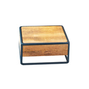 A small, square, wooden box crafted with rustic pine panels features a light brown finish and is encased in a thin black metal frame. Minimalist in design, the frame borders the box’s sides and base, set against a plain white background.
