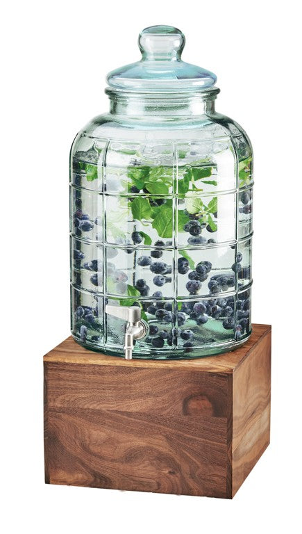 A clear 2 gallon beverage dispenser with a lid sits on a wooden stand. Filled with water, mint leaves, and whole blueberries, this glass beverage dispenser features a metal spigot on the front for easy pouring.