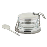 A small glass container with a metal lid and handle, set in a metal stand. This condiment jar set features a notch in the lid for the included silver spoon. The overall design is simple, modern, and dishwasher safe.