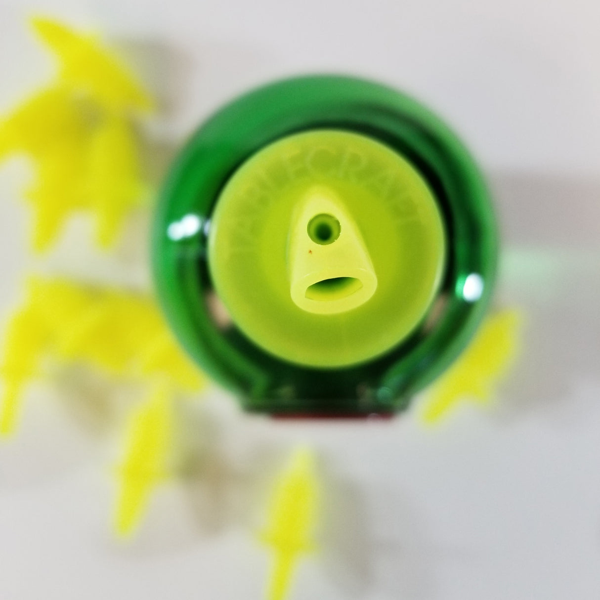 Top view of a green plastic lemon juice bottle with a yellow cap. The cap features a Free Flow Pourer and is labeled “TABLECRAFT.” Several yellow, leaf-shaped plastic pieces are scattered on a white surface next to the bottle.