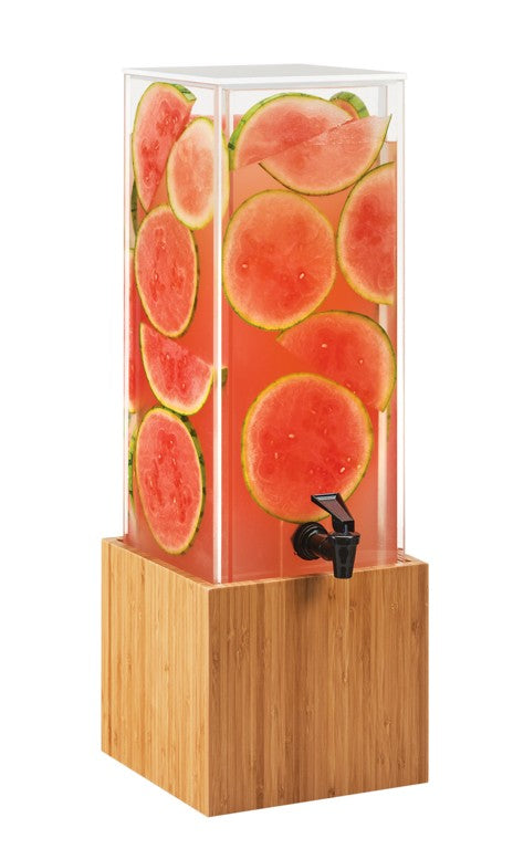 A tall, rectangular 3 gallon beverage dispenser with a wooden base is filled with pink liquid and large watermelon slices. The BPA free container has a black spout for pouring and displays fruit pressed against the clear sides.