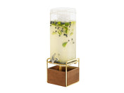 A tall, clear 3 gallon beverage dispenser filled with light yellow liquid, ice, lime slices, and blueberries stands on a gold metal frame with a wooden base and features a spigot for pouring drinks. The background is plain white.