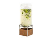 A 3 gallon beverage dispenser filled with light yellow liquid, lime slices, and blueberries sits on a metal stand with a wooden base. The dispenser has a spigot at the front and is topped with a clear plastic lid containing ice cubes.