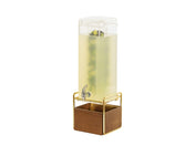 A tall, clear mid-century beverage dispenser with a 3 gallon capacity is filled with light yellow liquid and floating lemon and lime slices. It has a spigot near the bottom, sits on a wooden base with gold framing, against a plain white background.