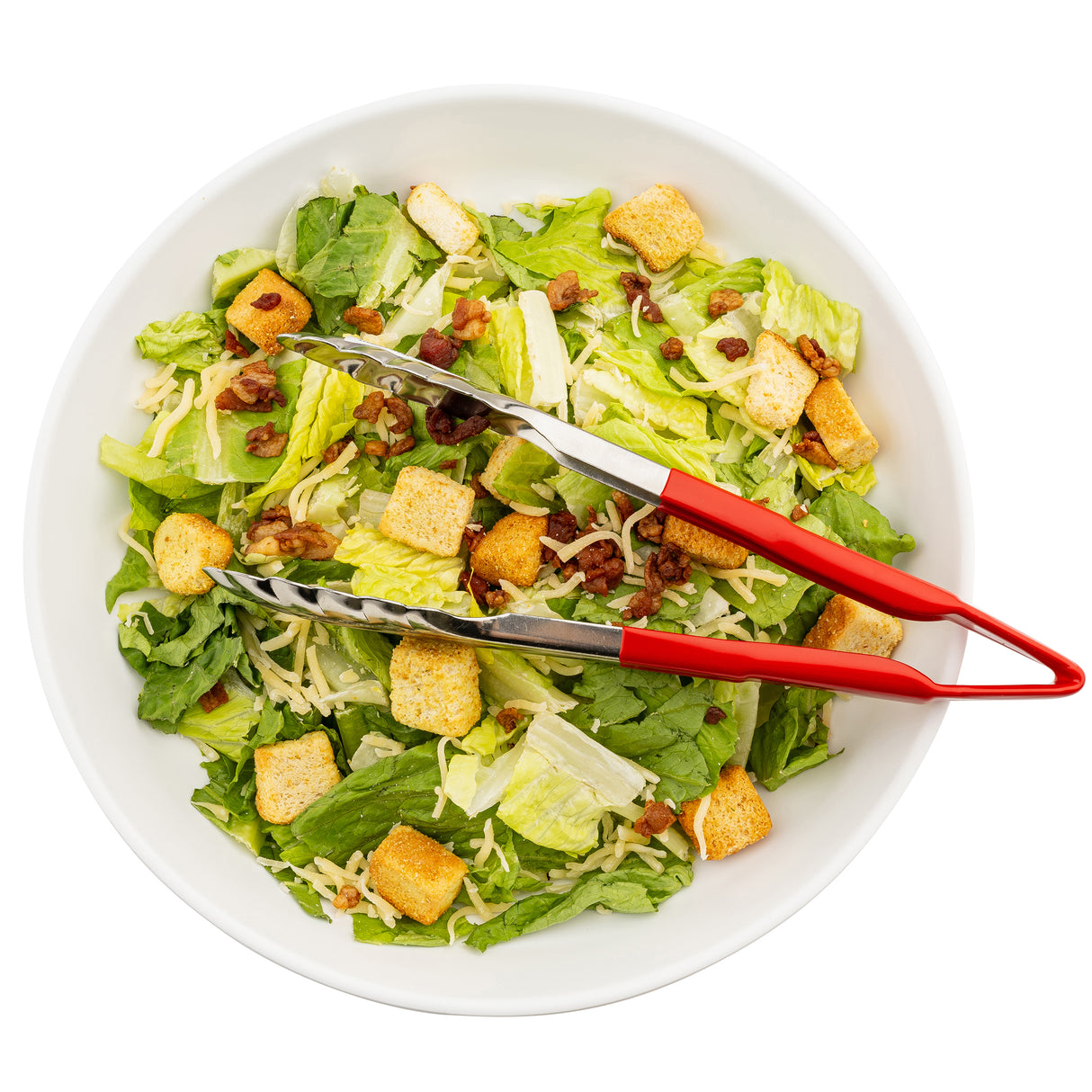 A white bowl filled with Caesar salad—romaine lettuce, croutons, shredded cheese, and bacon bits. Red-handled spring steel tongs rest atop the salad. The bowl is photographed from above against a white background.