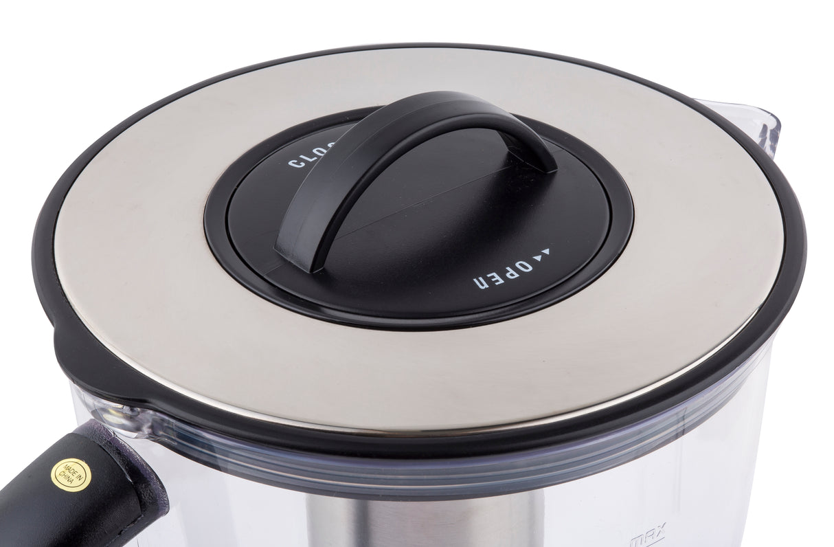 Close-up of a pitcher lid with a black handle and metallic silver top. The lid, made of stainless steel, features “OPEN” and “CLOSE” markers with arrows and is attached to a clear container with a black handle partially visible on the left.