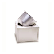 A metallic, brushed-steel insert pot is tilted and partially inserted into a square, white, modern counter-top unit with an opening on top, set against a plain white background. The minimalist design gives a contemporary and sleek appearance.