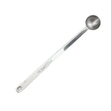 A stainless steel measuring spoon marked “1/2 tbsp / 7.5 ml.” The long handled spoon features a circular, deep bowl and a flat handle with a hole near the end for hanging. The image is set against a white background.