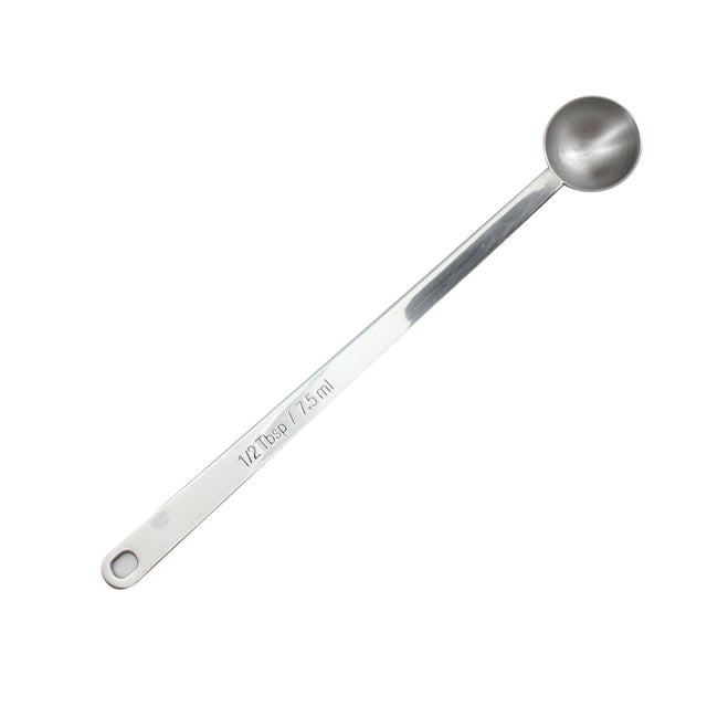 A stainless steel measuring spoon marked “1/2 tbsp / 7.5 ml.” The long handled spoon features a circular, deep bowl and a flat handle with a hole near the end for hanging. The image is set against a white background.