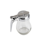 A clear teardrop glass syrup dispenser with a shiny silver metal lid and handle. The lid features a thumb lever for easy pouring. Mostly empty, it sits on a plain white background and is dishwasher safe for effortless cleaning.