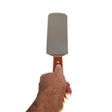 A hand holding a food turner with a rectangular stainless steel blade and a wood handle featuring a small hole near the top, shown against a white background.