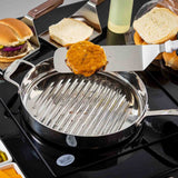 A stainless steel grill pan holds a cooked burger patty with melted cheese on a Food Turner featuring a stainless steel blade. Nearby are open burger buns, sliced onions, and condiments on a black stovetop, suggesting burger preparation in the kitchen.