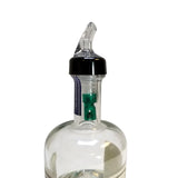 A clear glass bottle with a TableCraft black plastic Proper Pour spout and transparent angled nozzle. Inside the bottleneck is a green 3/4 oz pourer. The image is set against a plain white background, focusing on the bottle’s top portion.