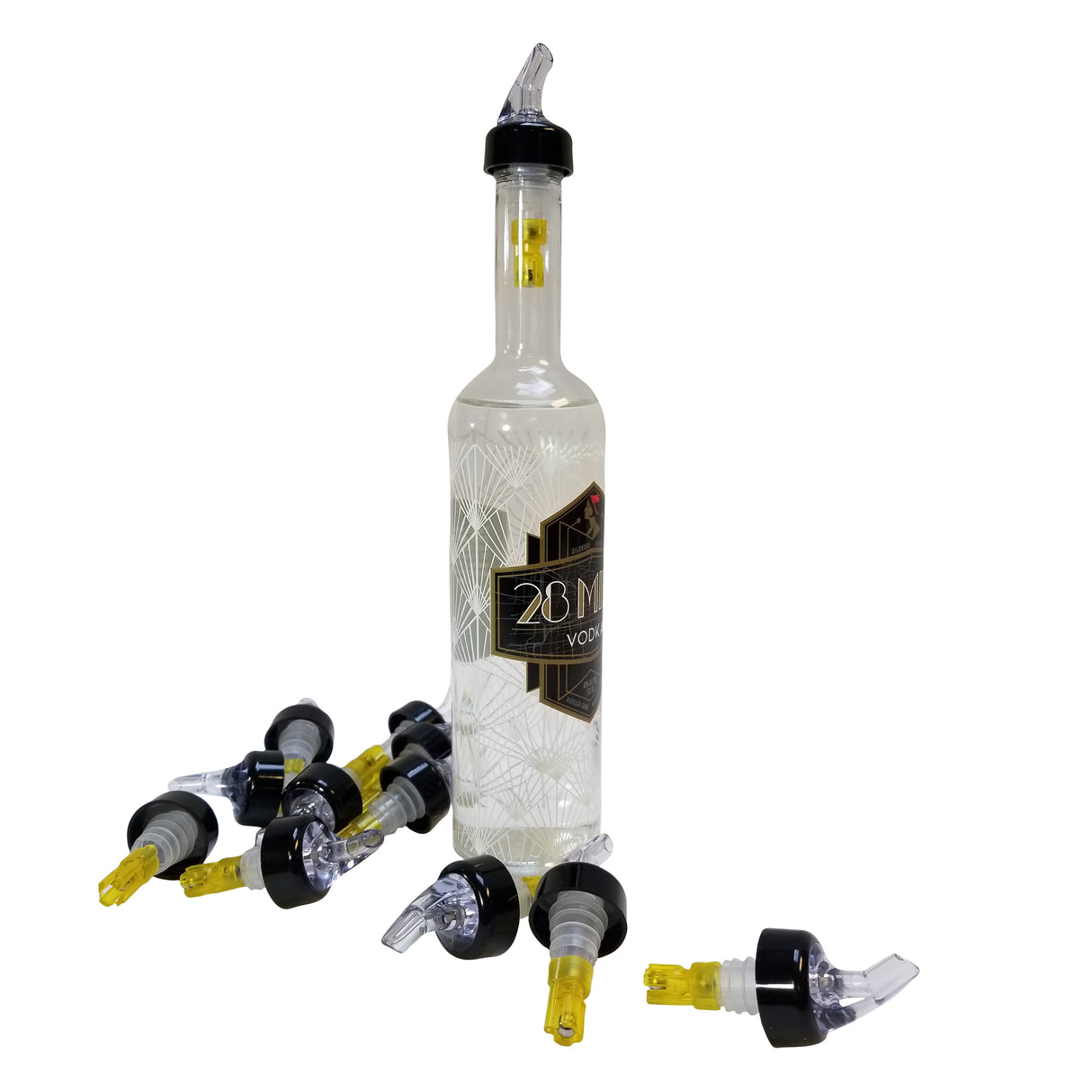 A clear 28M vodka bottle with a Proper Pour 1-1/2 oz. spout stands upright. Surrounding its base are eight black and yellow pour spouts scattered on a white surface. The bottle features a geometric pattern and black label, ideal for Cash & Carry shelves.