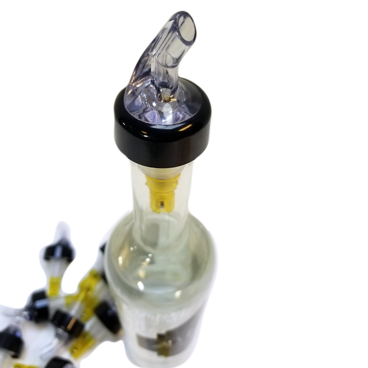 A Proper Pour 1-1/2 oz. pour spout with a black collar and angled transparent nozzle is inserted into the top of a glass bottle. More identical pour spouts are arranged to the left, all shown on a white background with a clean, clinical feel.