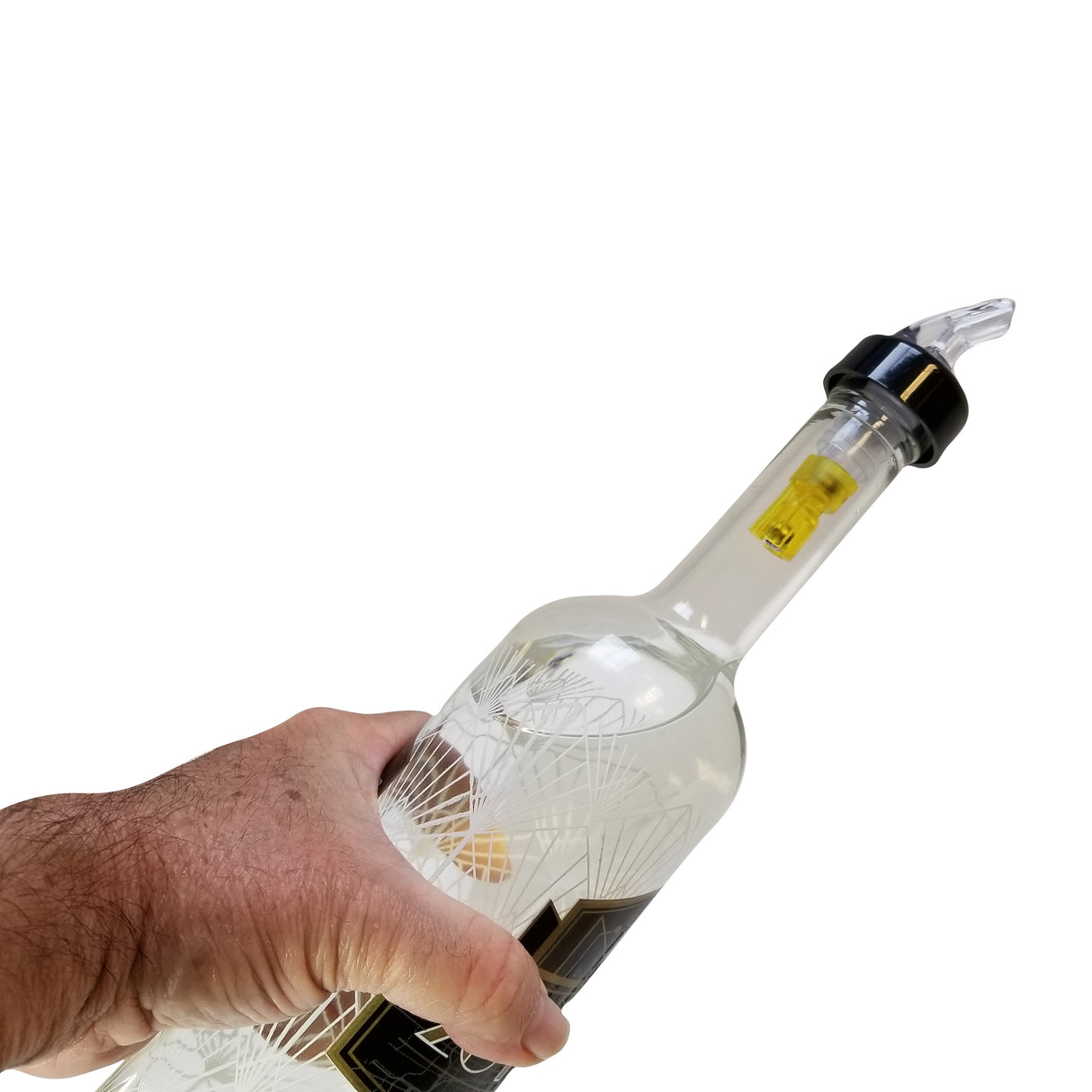 A hand holds a clear bottle with an intricate white geometric design and a black and yellow Proper Pour 1-1/2 oz. spout against a plain white background. The bottle is angled as if ready to pour, ideal for any Cash & Carry setup.
