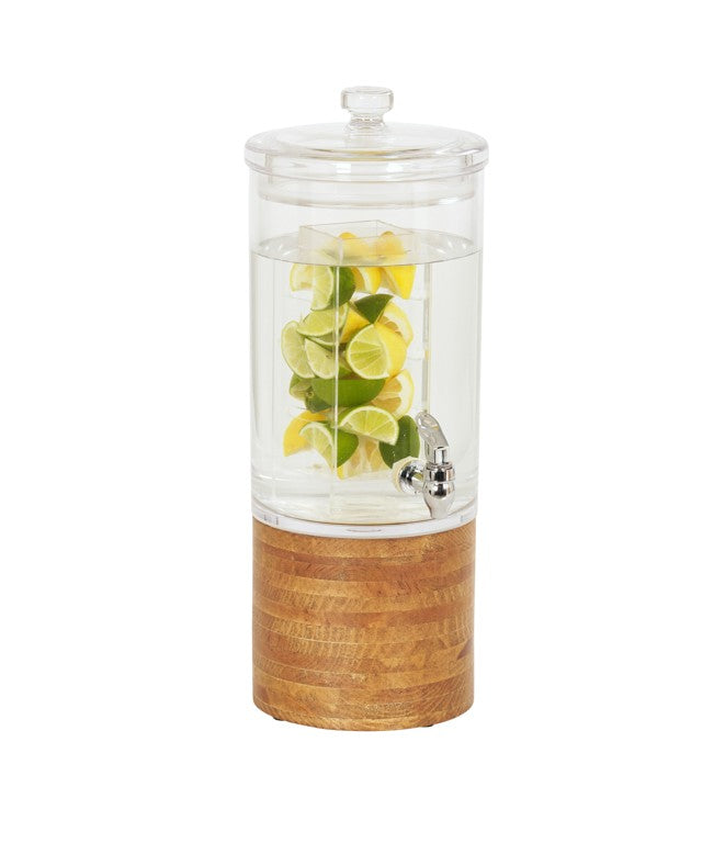 A clear glass beverage dispenser with an infusion chamber, lid, and spigot is filled with water and slices of lemon and lime. The dispenser sits on a round wood base, all set against a plain white background.