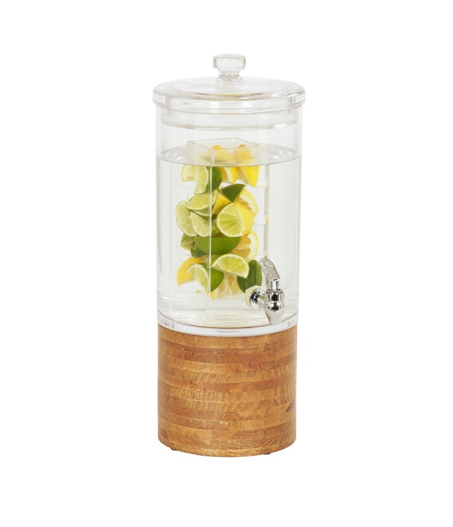 A clear glass beverage dispenser with an infusion chamber, lid, and spigot is filled with water and slices of lemon and lime. The dispenser sits on a round wood base, all set against a plain white background.