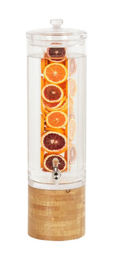 A tall, clear 3 gallon Madera Beverage Dispenser with a wooden base features an infusion chamber packed with orange, blood orange, and lemon slices. The dispenser includes a silver spout near the bottom and a clear lid on top.