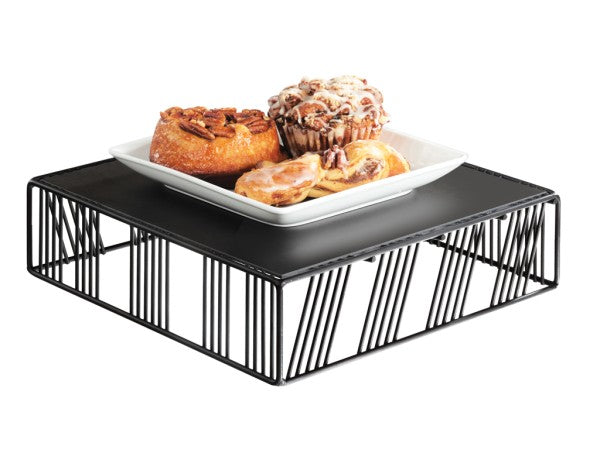 A square black Portland Riser wire stand holds a black platform topped with a white square plate. On the plate are three pastries: a pecan sticky bun, a cinnamon roll with frosting, and a danish pastry. The background is white.