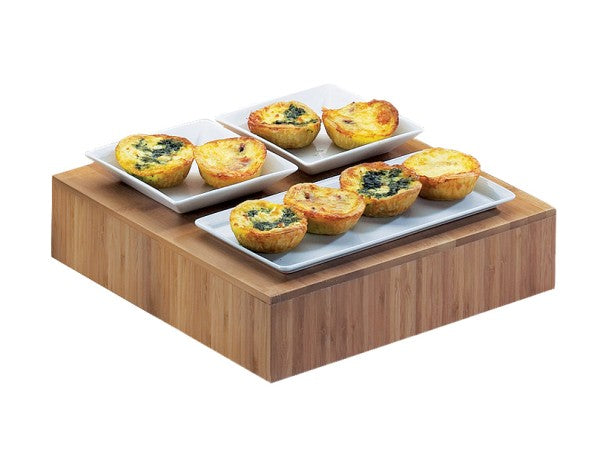 Three rectangular white plates with six mini quiches, some with spinach toppings, are displayed on a Cal-Mil bamboo display tray. The golden-brown quiches are neatly arranged in pairs on each plate against a white background.
