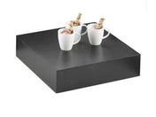 A large, square Cal-Mil Midnight Bamboo Display Tray holds three white mugs, each filled with a dessert topped with a wafer stick. The plain white backdrop highlights the striking contrast between the dark display riser and the white mugs.