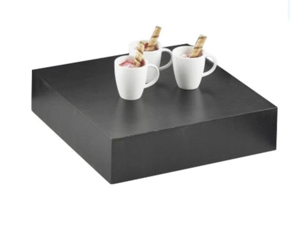A large, square Cal-Mil Midnight Bamboo Display Tray holds three white mugs, each filled with a dessert topped with a wafer stick. The plain white backdrop highlights the striking contrast between the dark display riser and the white mugs.